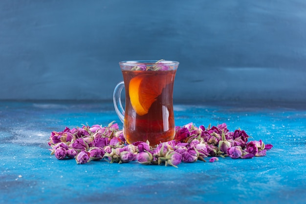Vaso de té con rosas en ciernes colocadas sobre la mesa azul.