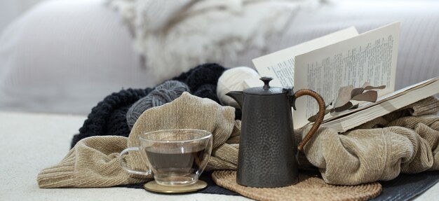 Vaso de té, tetera y libro sobre un espacio borroso de luz en colores fríos.