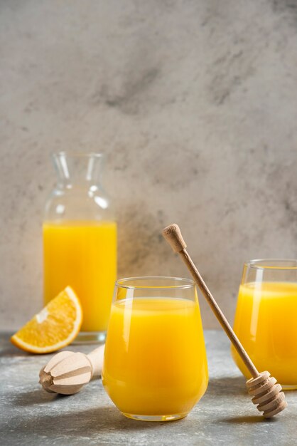 Un vaso de vasos de jugo de naranja y un cucharón de madera.