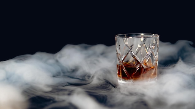 Vaso de whisky en una mesa cubierta de humo contra un fondo negro