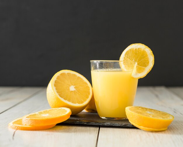 Vaso de zumo de naranja y rodajas de fruta en pizarra