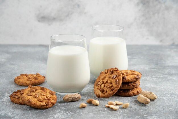 Vasos de leche y galletas caseras con maní orgánico sobre mesa de mármol.