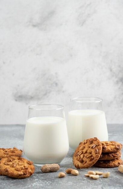 Vasos de leche y galletas caseras con maní orgánico sobre mesa de mármol.