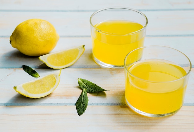Vasos de refrescante bebida amarilla cerca de limón y menta
