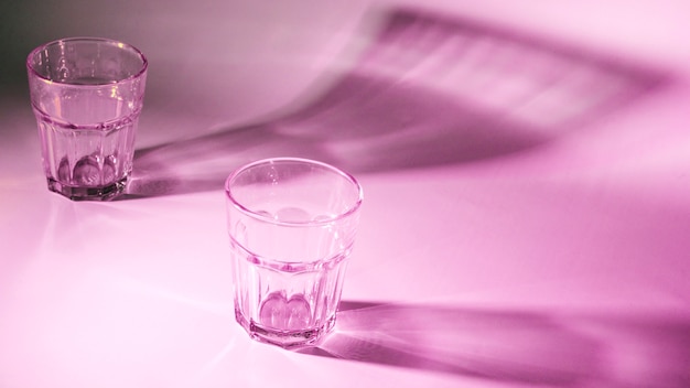 Un vasos vacíos con sombra oscura sobre fondo rosa