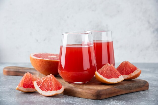 Vasos de vidrio de jugo de toronja fresca con rodajas de frutas colocadas sobre tabla de madera.