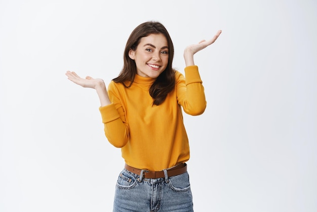 Vaya, mi error Linda chica tonta levantando las manos y encogiéndose de hombros confundida sonriendo como siendo un poco culpable no sé cómo sucedió de pie contra el fondo blanco