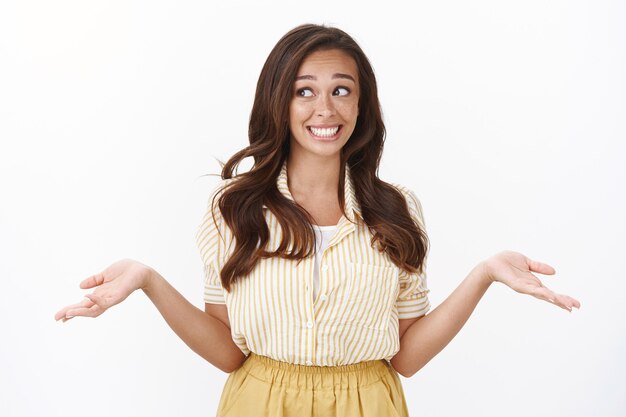 Vaya, niña evitando el contacto visual para no dejarse sorprender mintiendo. Novia joven tonta encogiéndose de hombros con las manos extendidas hacia los lados, sonriendo culpable y mirando hacia otro lado, tratando de convencer de que no tiene idea de lo que sucedió.