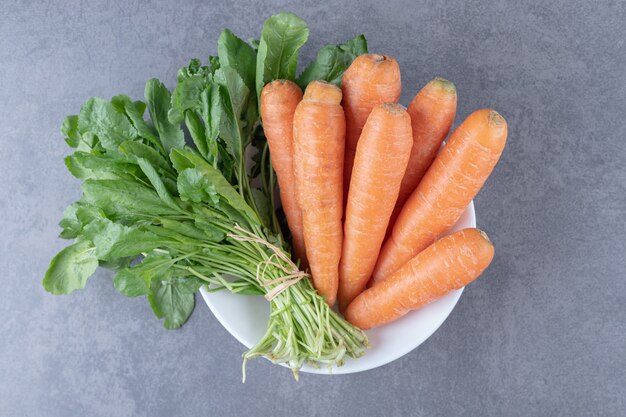 Vegetal verde con zanahoria en un bol, sobre la superficie de mármol.