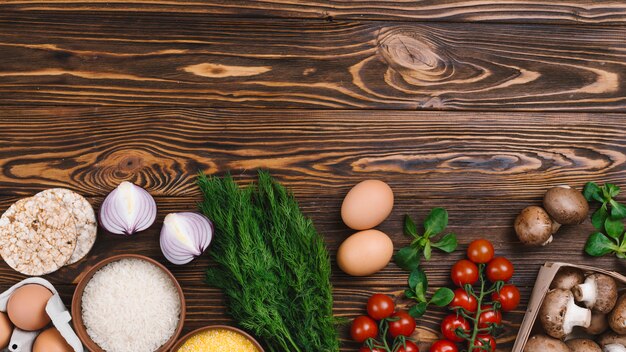 Vegetales frescos; Huevos y granos de arroz y pastel de arroz inflado sobre mesa de madera