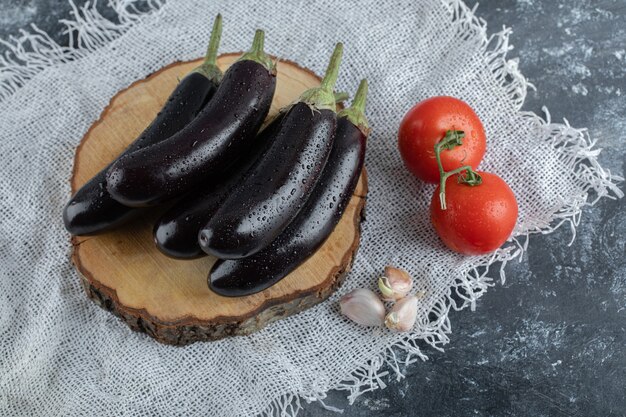 Vegetales orgánicos. Berenjenas moradas sobre tabla de madera con tomate y ajo.