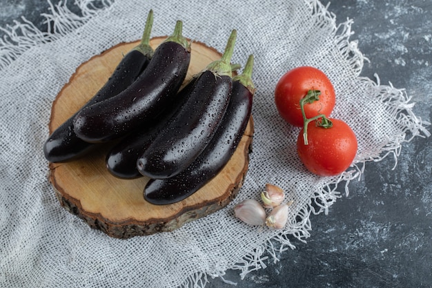 Vegetales orgánicos. Berenjenas moradas sobre tabla de madera con tomate y ajo.