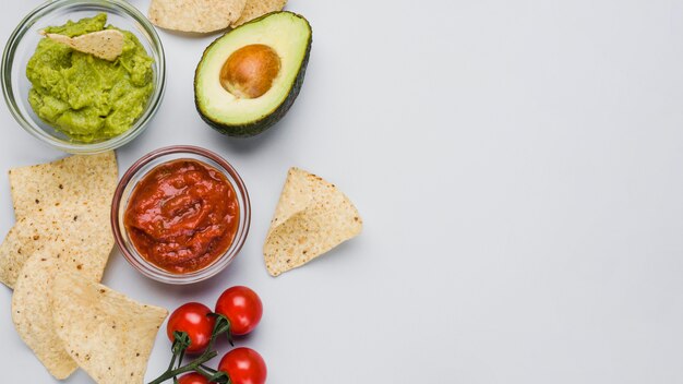 Vegetales y salsas en cuencos de vidrio entre nachos.