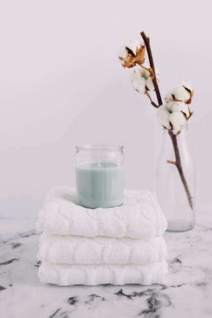 Foto gratuita vela en candelabro sobre servilletas blancas apiladas cerca de una ramita de algodón en una botella