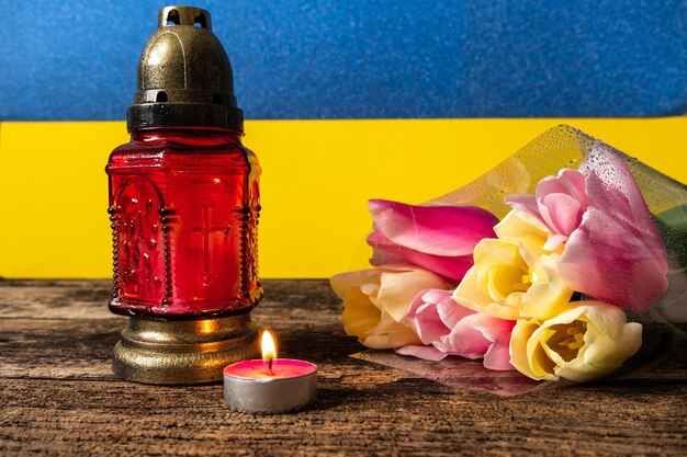 Una vela encendida con una lámpara roja conmemorativa y un ramo de tulipanes amarillos y rosas en la oscuridad
