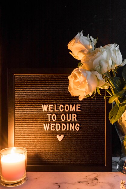 Vela encendida y rosas cerca del marco negro con la bienvenida a nuestro mensaje de boda