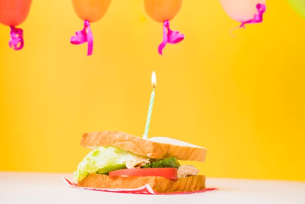 Vela encendida sobre el sandwich contra el fondo amarillo