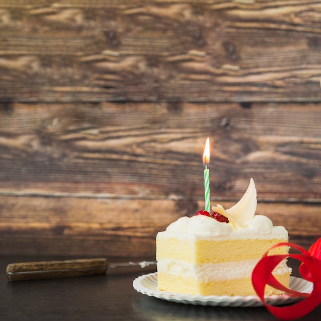 Vela iluminada sobre la rebanada de la torta en el plato sobre la mesa de madera