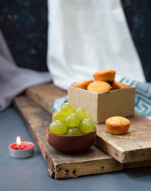 Vela roja, una caja de muffins y uvas verdes en un trozo de madera