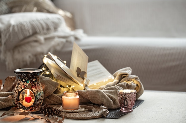 Velas en candelabros, libro, sweater, guirnalda en el espacio luminoso del living.