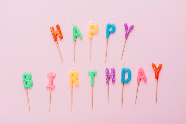 Velas coloridas del feliz cumpleaños con el palillo en fondo rosado