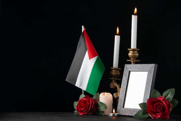 Velas encendidas con bandera palestina y flores en la superficie oscura