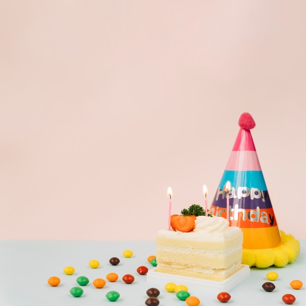 Velas encendidas en el pastel; caramelos y sombrero de cumpleaños contra fondo de color