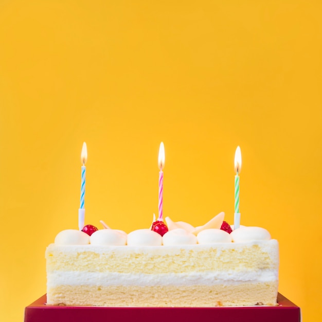 Foto gratuita velas encendidas en pastel dulce sobre fondo amarillo