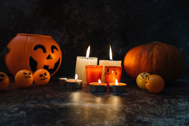 Velas encendidas de pie entre canasta de naranja y calabaza y bolas en la foto