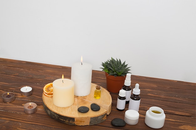 Una velas encendidas; rodajas de cítricos secos; el último; Miel y botellas de aceite esencial en una maceta sobre el escritorio contra la pared