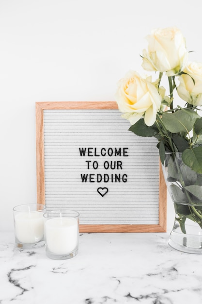 Foto gratuita velas y florero con tablero de bienvenida para boda contra fondo blanco