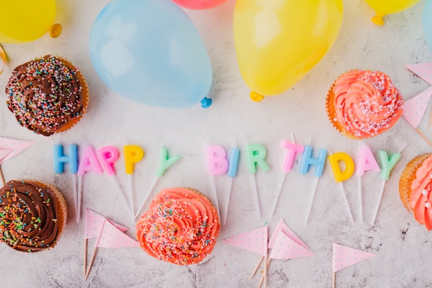 Velas en forma de letra en medio de cupcakes y globos