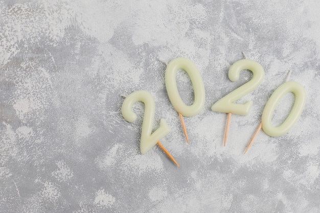 Velas en forma de números 2020 como símbolo del año nuevo junto a dulces con forma de navidad en una mesa gris. Vista superior, endecha plana