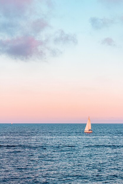 Velero navegando en el océano ondulado bajo el hermoso cielo nublado rosa