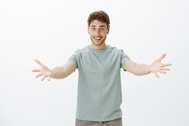 Ven a mí, déjame abrazarte. Retrato de lindo hombre de aspecto amistoso en traje casual, tirando de los brazos hacia y sonriendo ampliamente