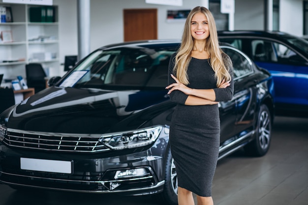 Vendedor femenino en una sala de exposición de automóviles junto al automóvil