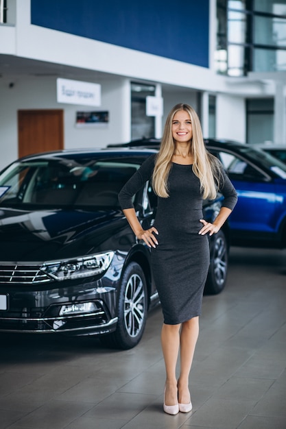 Vendedor femenino en una sala de exposición de automóviles junto al automóvil