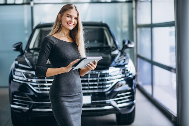 Vendedor femenino en una sala de exposición de automóviles junto al automóvil