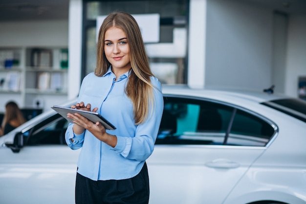 Vendedor femenino en una sala de exposición de automóviles junto al automóvil