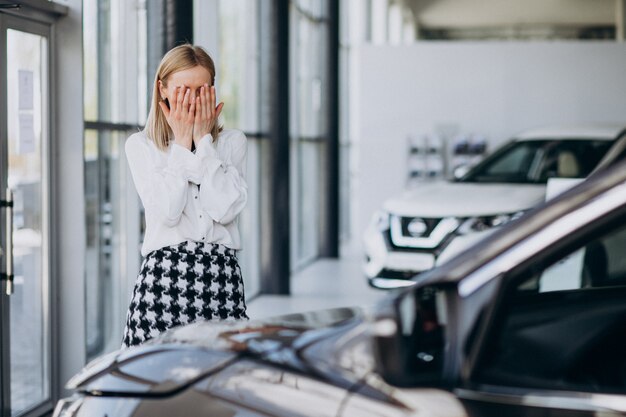 Vendedor femenino en una sala de exposición de automóviles de pie junto al coche