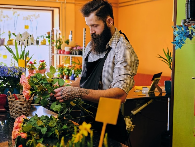 El vendedor de flores con estilo barbudo tiene rosas rosas en una tienda de mercado.