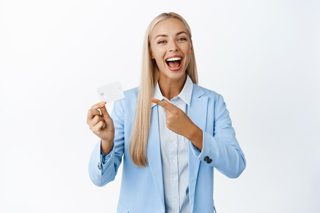Vendedora sonriente señalando el banco de publicidad de tarjetas de crédito de pie en traje sobre fondo blanco Concepto de finanzas