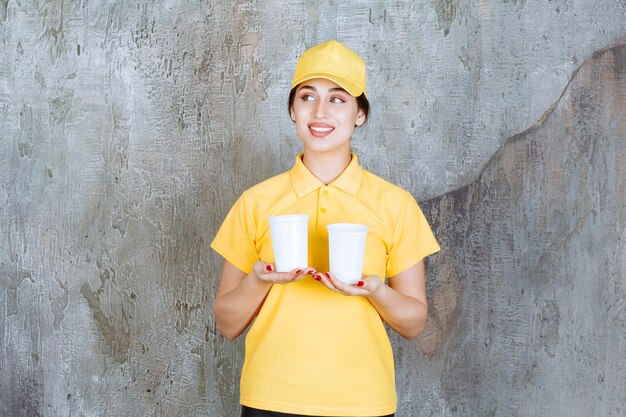 Una vendedora en uniforme amarillo sosteniendo dos vasos de plástico de bebida
