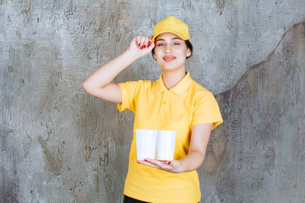 Una vendedora en uniforme amarillo sosteniendo dos vasos de plástico de bebida