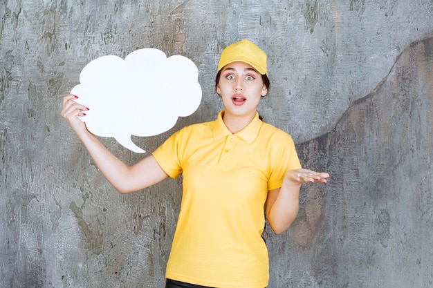 Foto gratuita una vendedora en uniforme amarillo sosteniendo un tablero de información en forma de nube y parece confundida y aterrorizada