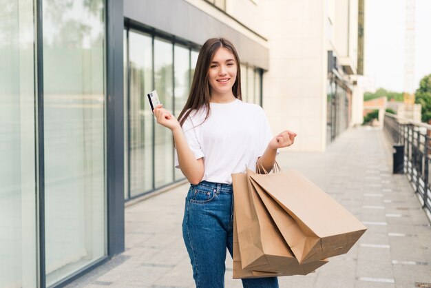 Venta y turismo, concepto de gente feliz - hermosa mujer con tarjeta de crédito con bolsas de compras en el ctiy