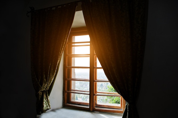 Ventana antigua de madera con cortinas en una habitación oscura con luz solar