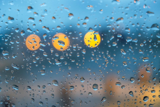 Ventana de vidrio cubierta de gotas de lluvia con luces en el fondo borroso