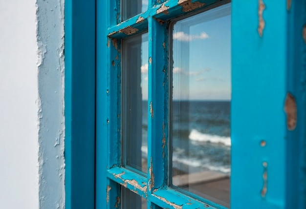Ventana con vista al mar y pintura azul desprendida