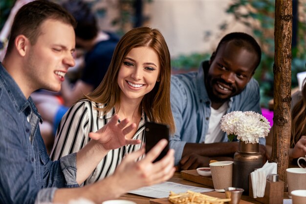 Ver fotos divertidas en el teléfono inteligente en la reunión informal informal con amigos cercanos